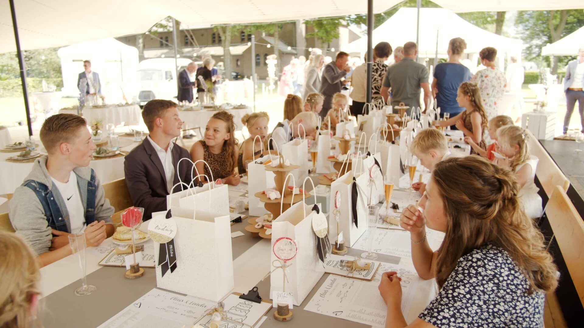 Viele Kinder sitzen an einem Tisch auf einer Bierzeltgarnitur bei einer Hochzeit.