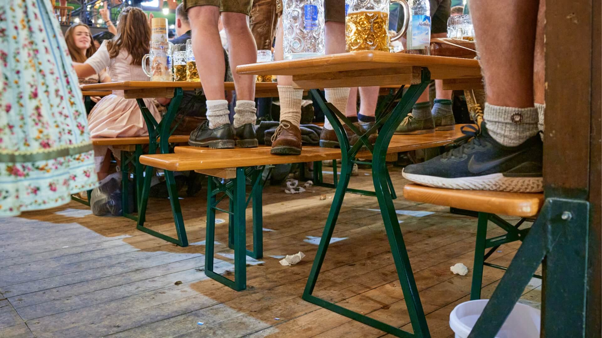 Mehrere Personen stehen beim Oktoberfest auf den Bierbänken der Bierzeltgarnitur mit Beinfreiheit.