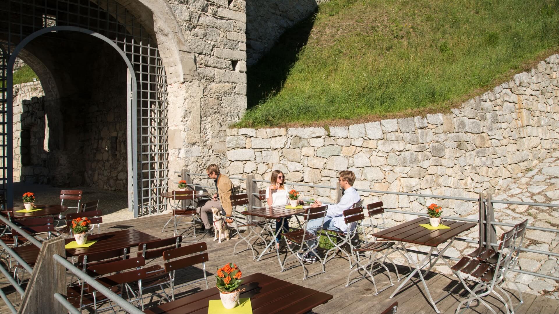 A few people sit outside on the rectangular beer garden furniture and enjoy the sun.