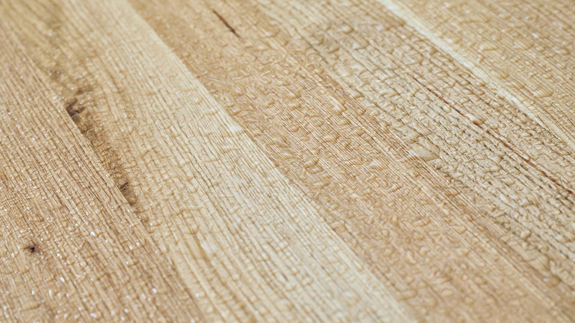 Designgarnitur Lago mit Wassertropfen auf der Oberfläche des Holzes. Die UV-Lasur schützt die Tischplatte vor Verformungen und Verfärbungen. Das Set ist somit witterungsbeständig und schwer entflammbar.