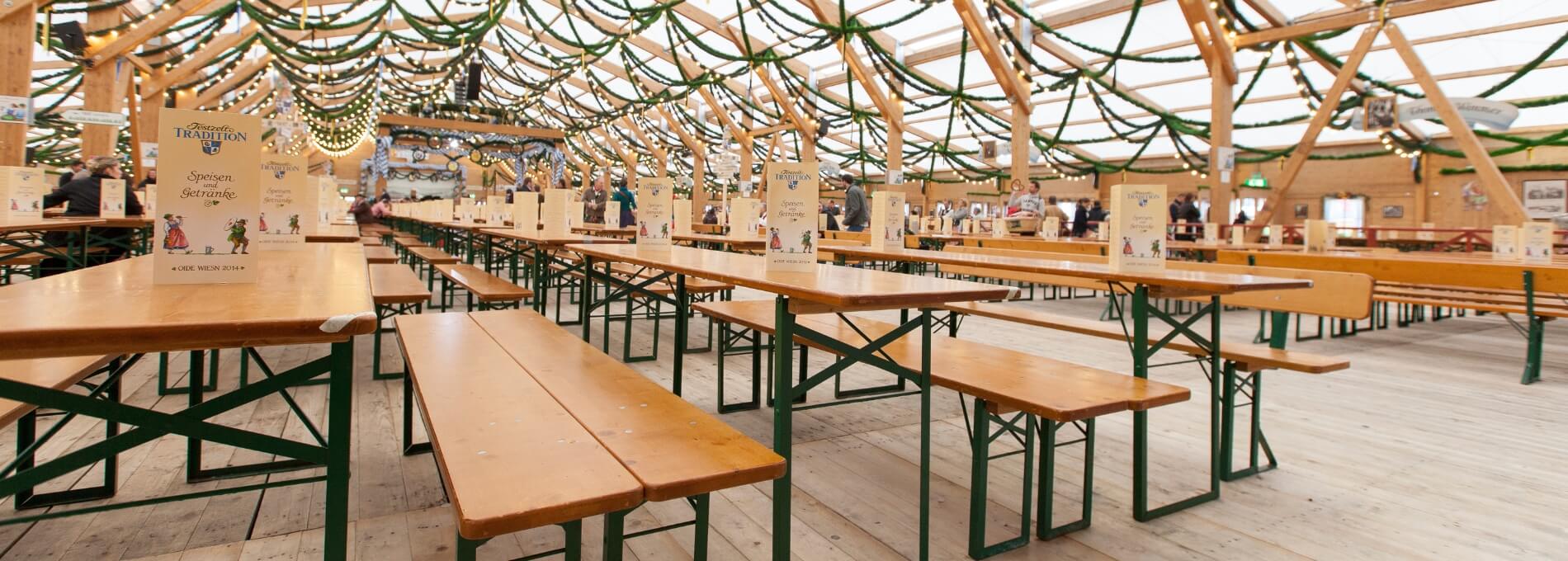 Viele Tische und Bänke der Bierzeltgarnitur unter einem Festzelt beim Oktoberfest.