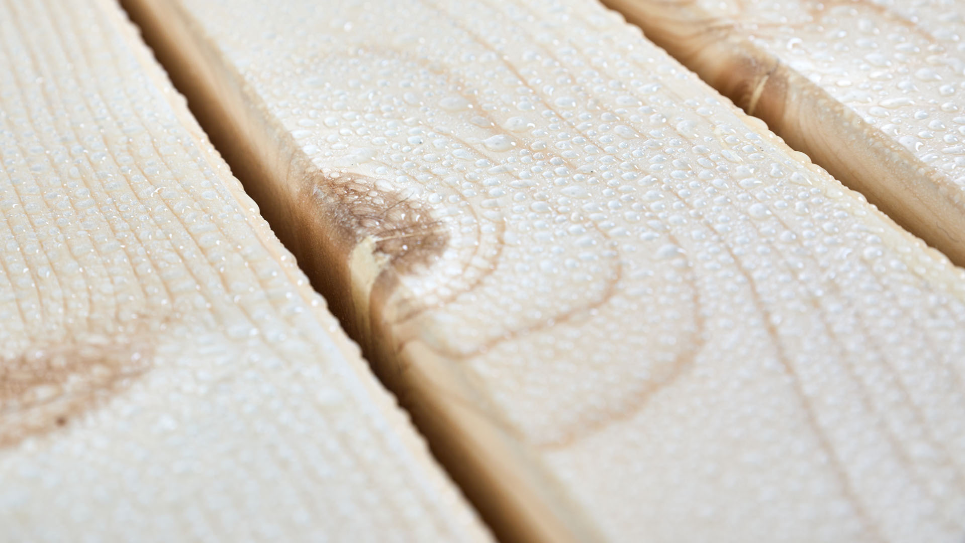 Designgarnitur SitDown mit Wassertropfen auf der Oberfläche des Holzes. Die UV-Lasur schützt die Tischplatte vor Verformungen und Verfärbungen. Das Set ist somit witterungsbeständig und schwer entflammbar.