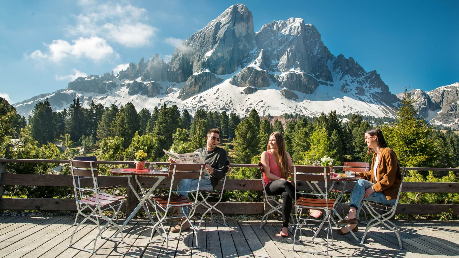 Mehrere Personen sitzen auf einer Terrasse auf den Biergartenmöbel mit Blick auf die Berge.