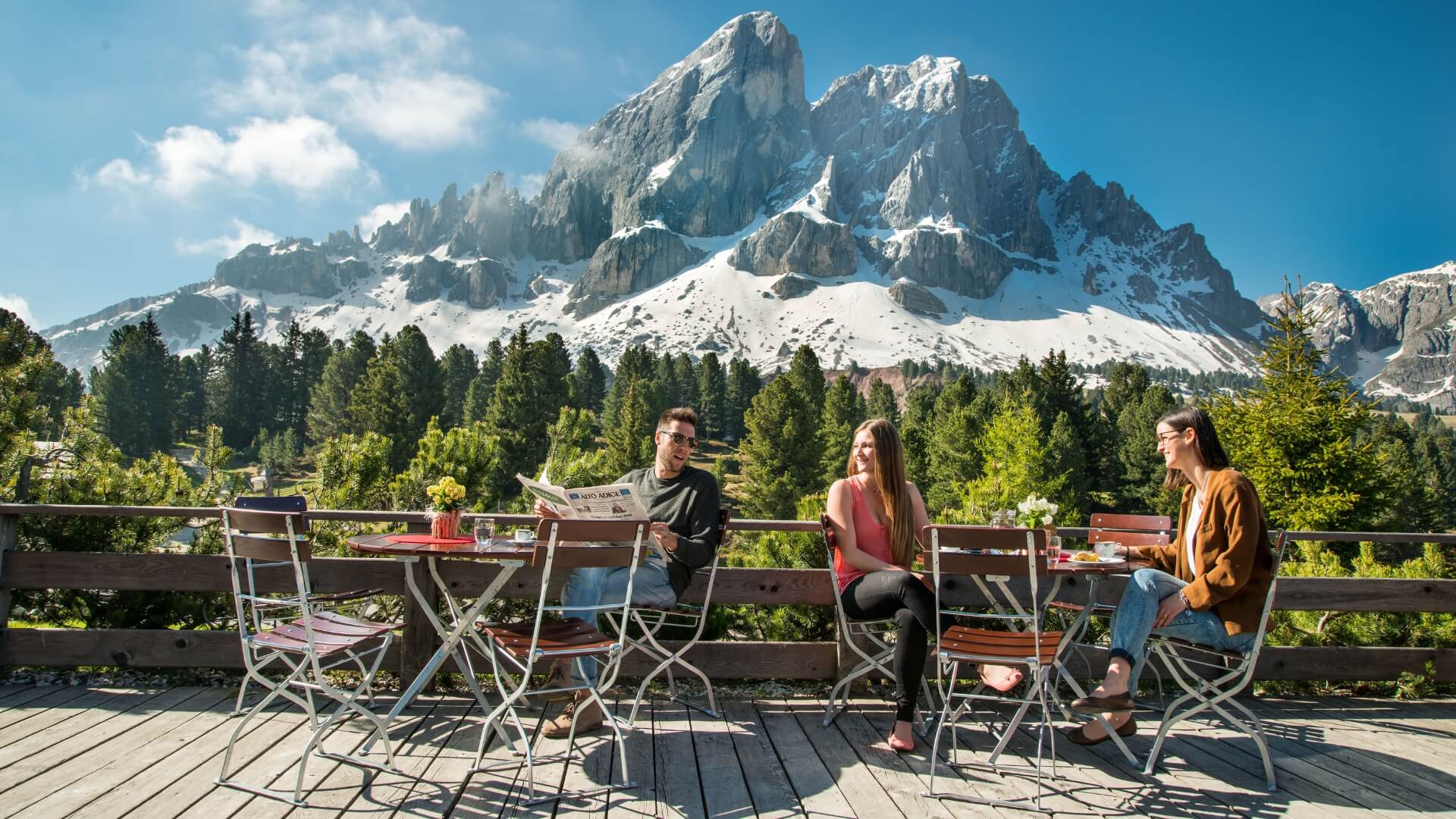 Several people sitting on a terrace on the beer garden furniture with a view of the mountains.