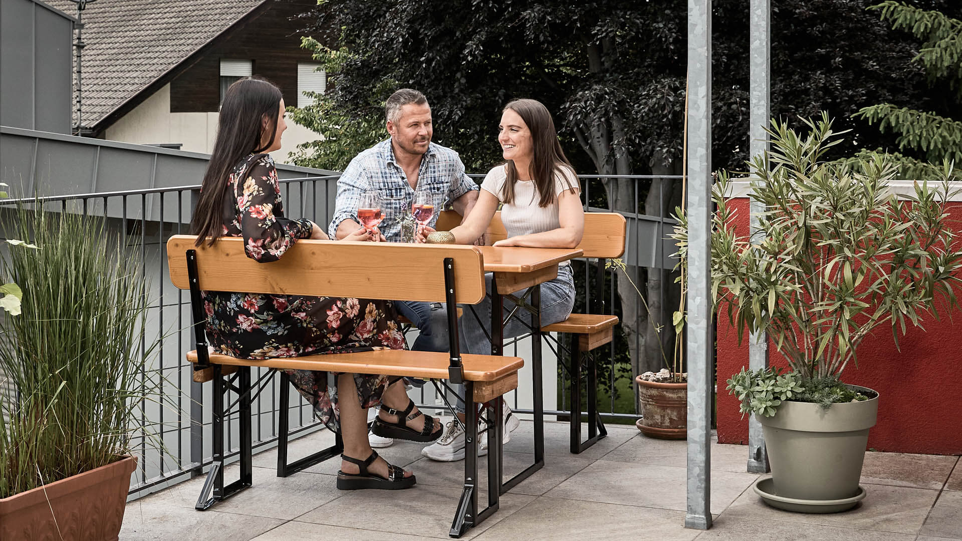 Three people sitting on the small beer garden table set Shorty with backrest on a balcony.