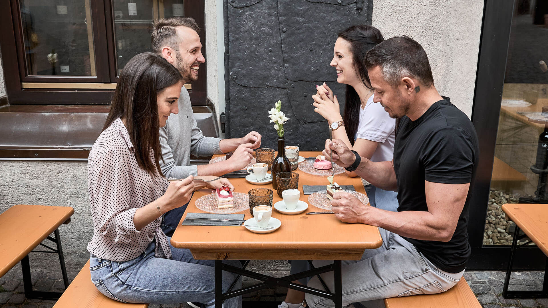 Four people sitting on the small beer garden table set in the outdoor area of a restaurant.