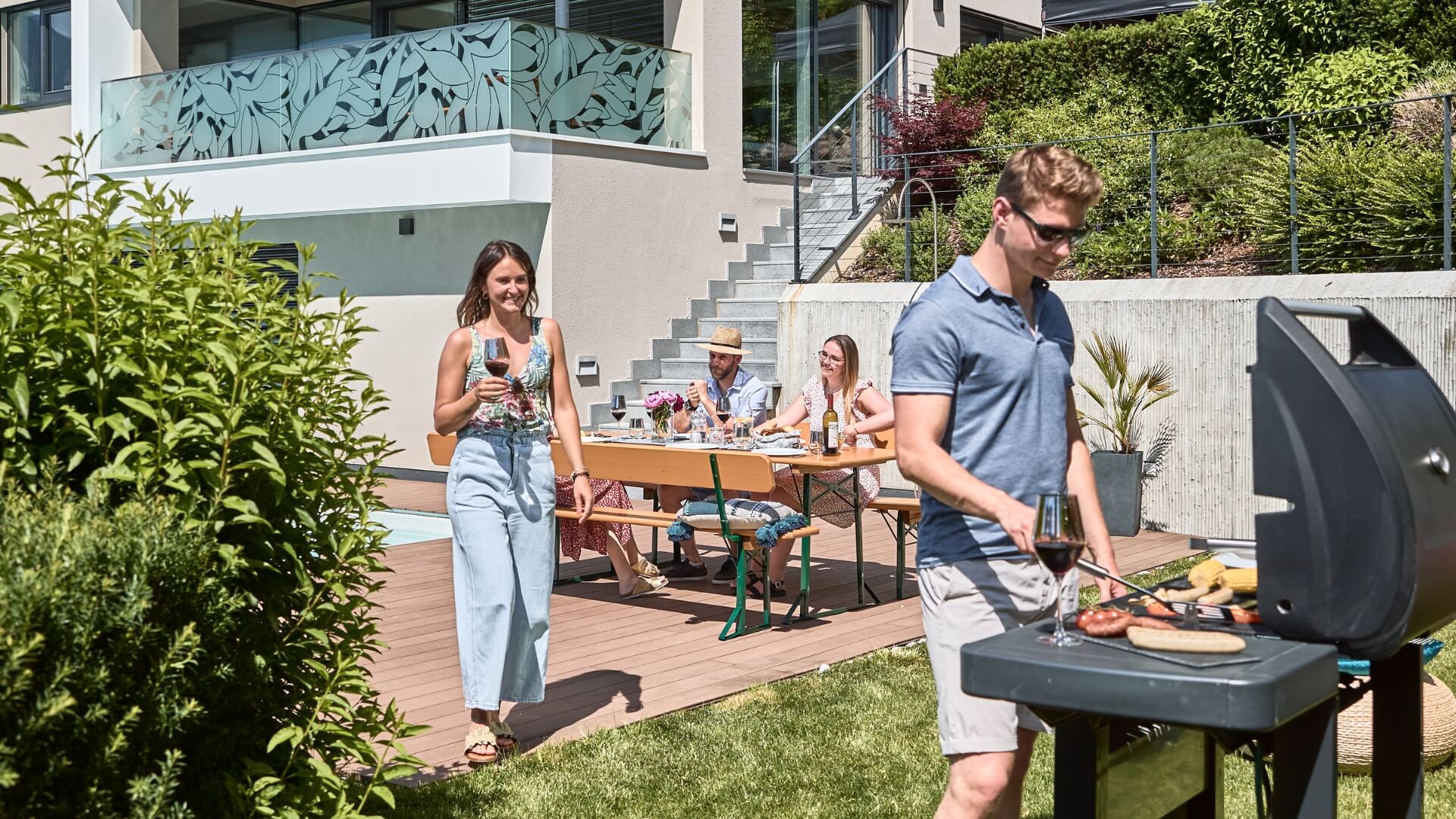 A barbecue party is taking place in the garden and the wide beer garden table set with backrest is used to relax.