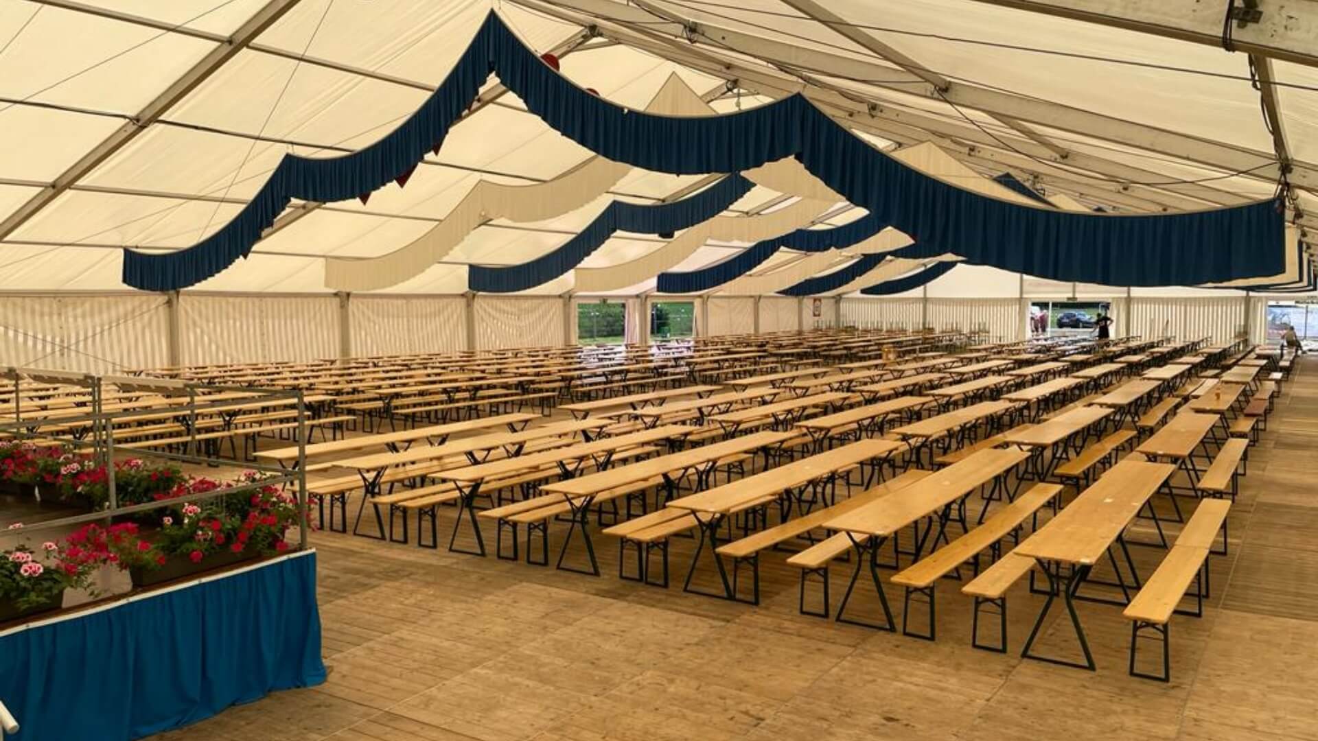 Many beer garden table sets with legroom are placed in a marquee.