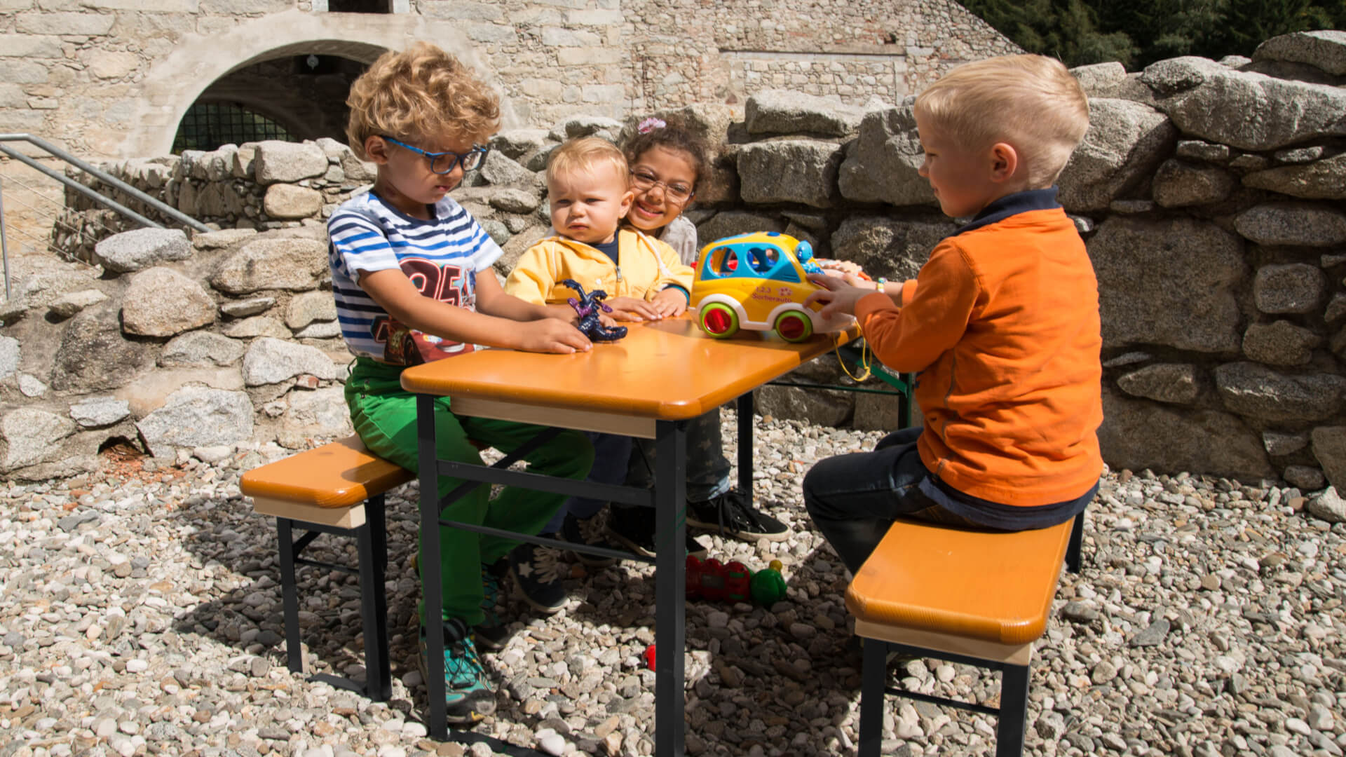 Vier kleine Kinder sitzen auf der Bierzeltgarnitur Bambini und spielen miteinander. 