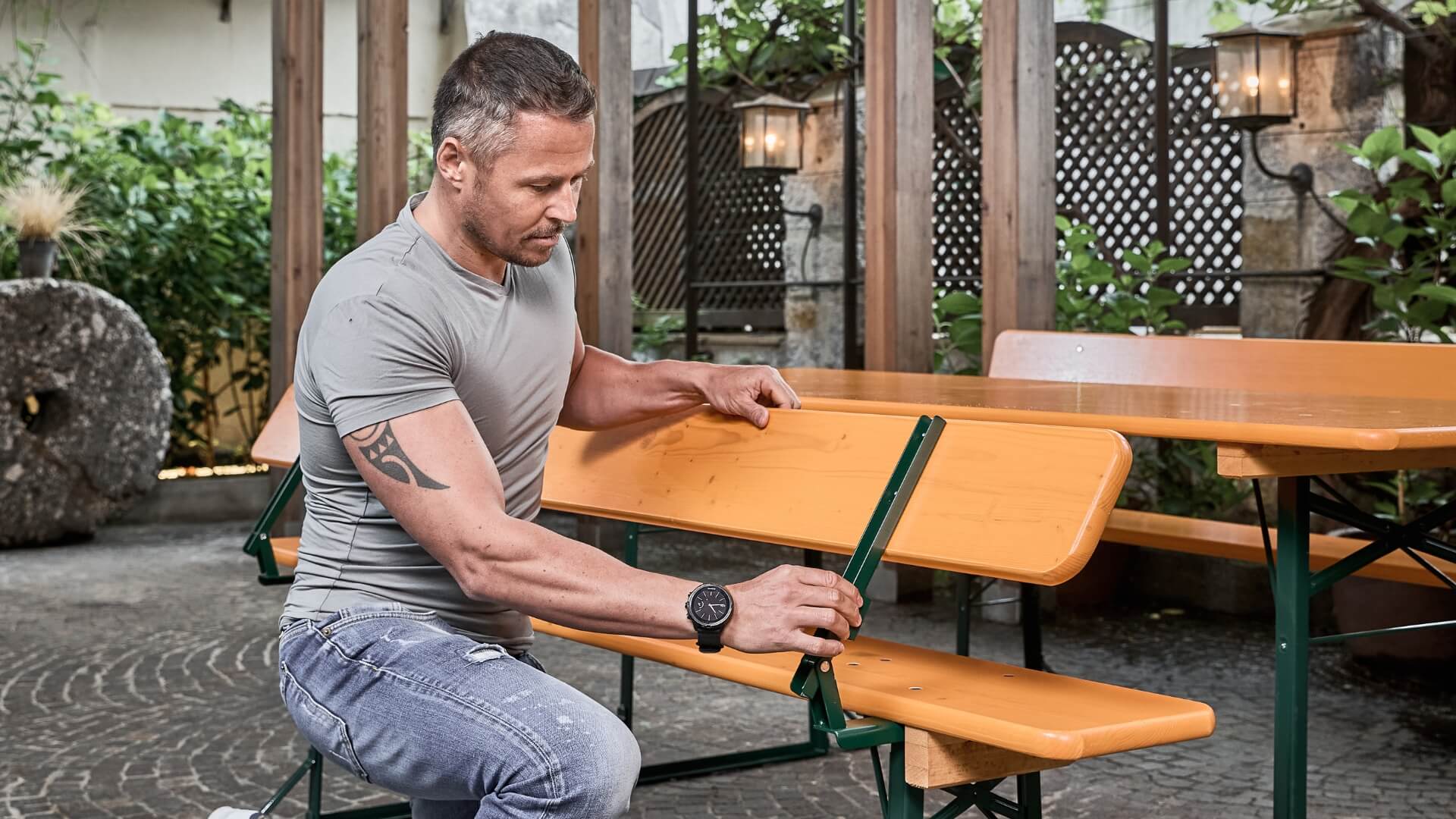 A boy presses the bolt at the back of the classic beer garden table set to be able to fold the backrest.