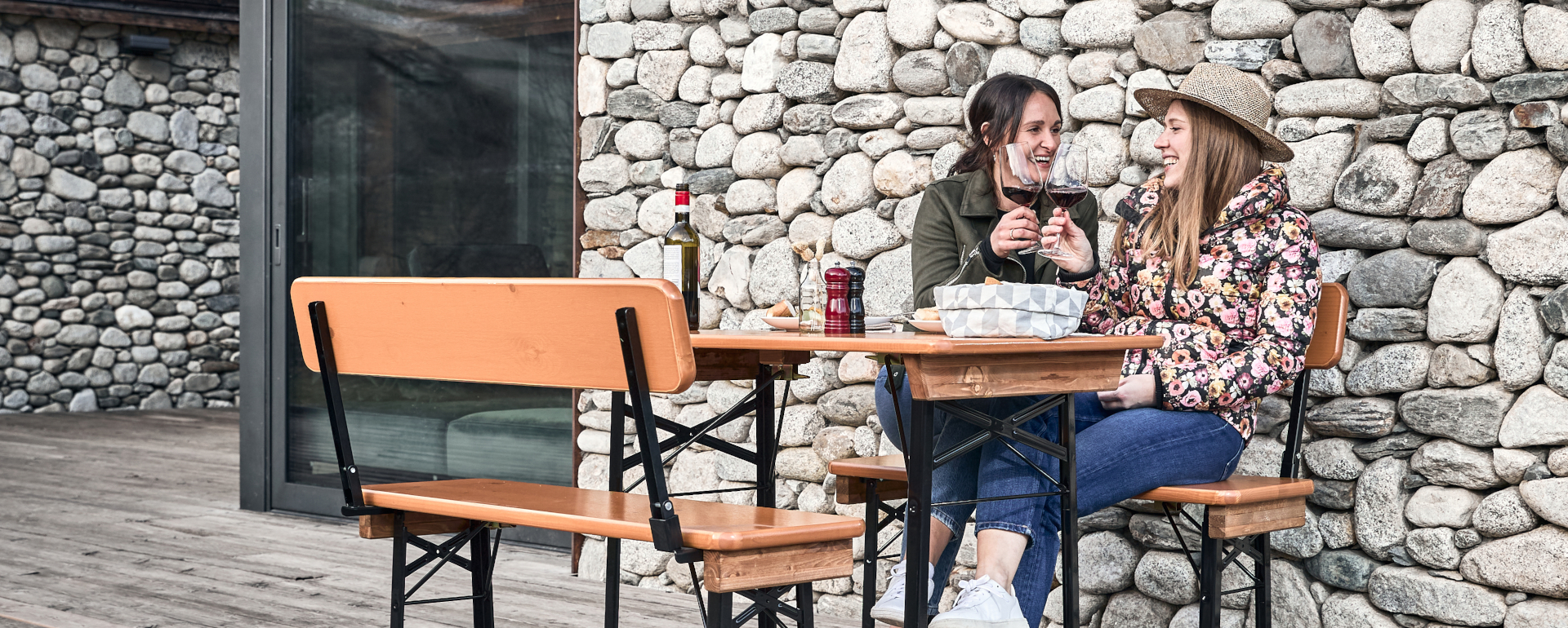 Zwei Freundinnen sitzen auf der kurzen Bierzeltgarnitur mit Lehne und stoßen an.