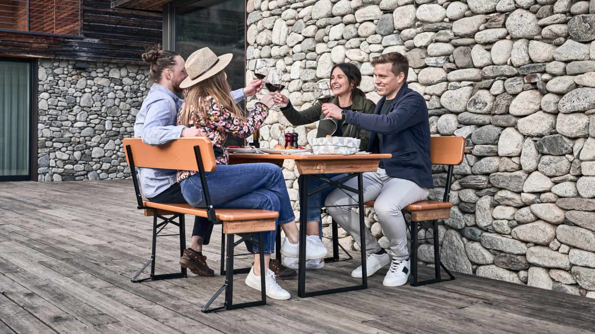 Vier Personen essen zu Mittag auf einer kleinen Bierzeltgarnitur mit Lehne auf der Terrasse.