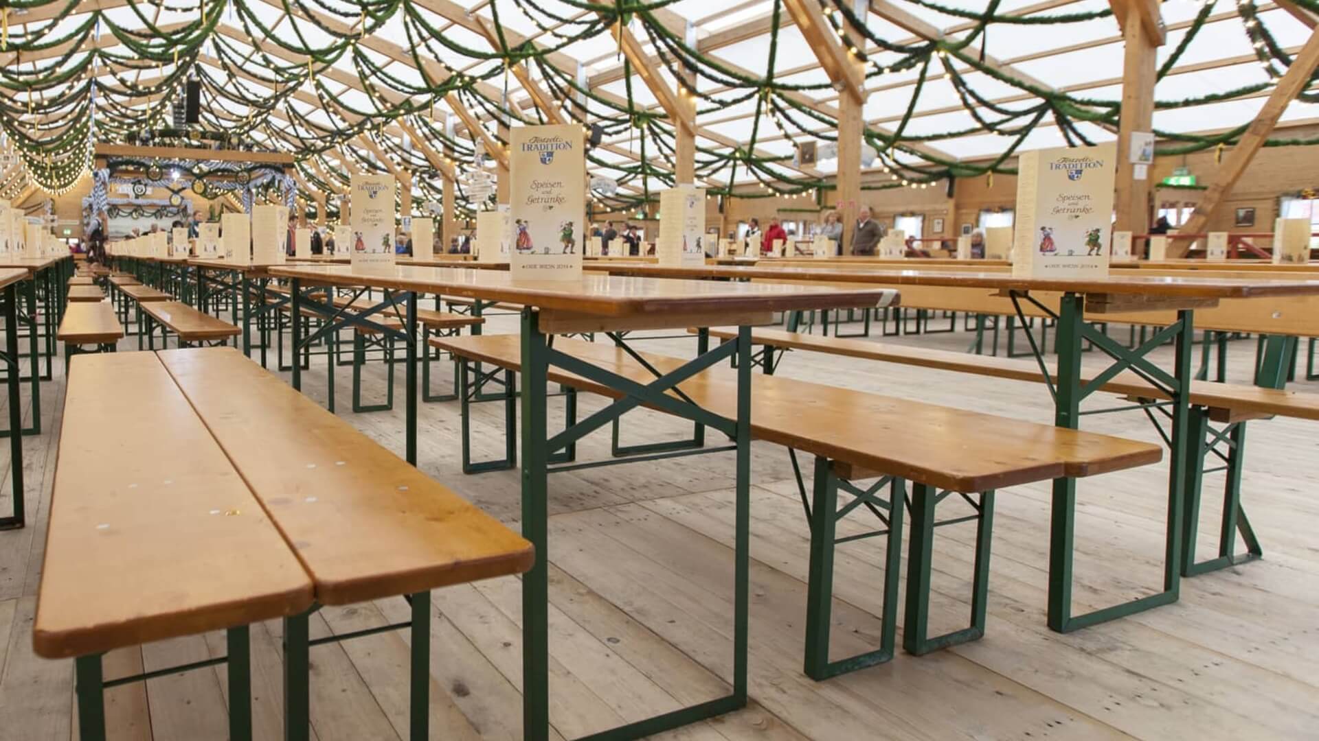 Viele Tische und Bänke der Bierzeltgarnitur unter einem Festzelt beim Oktoberfest.