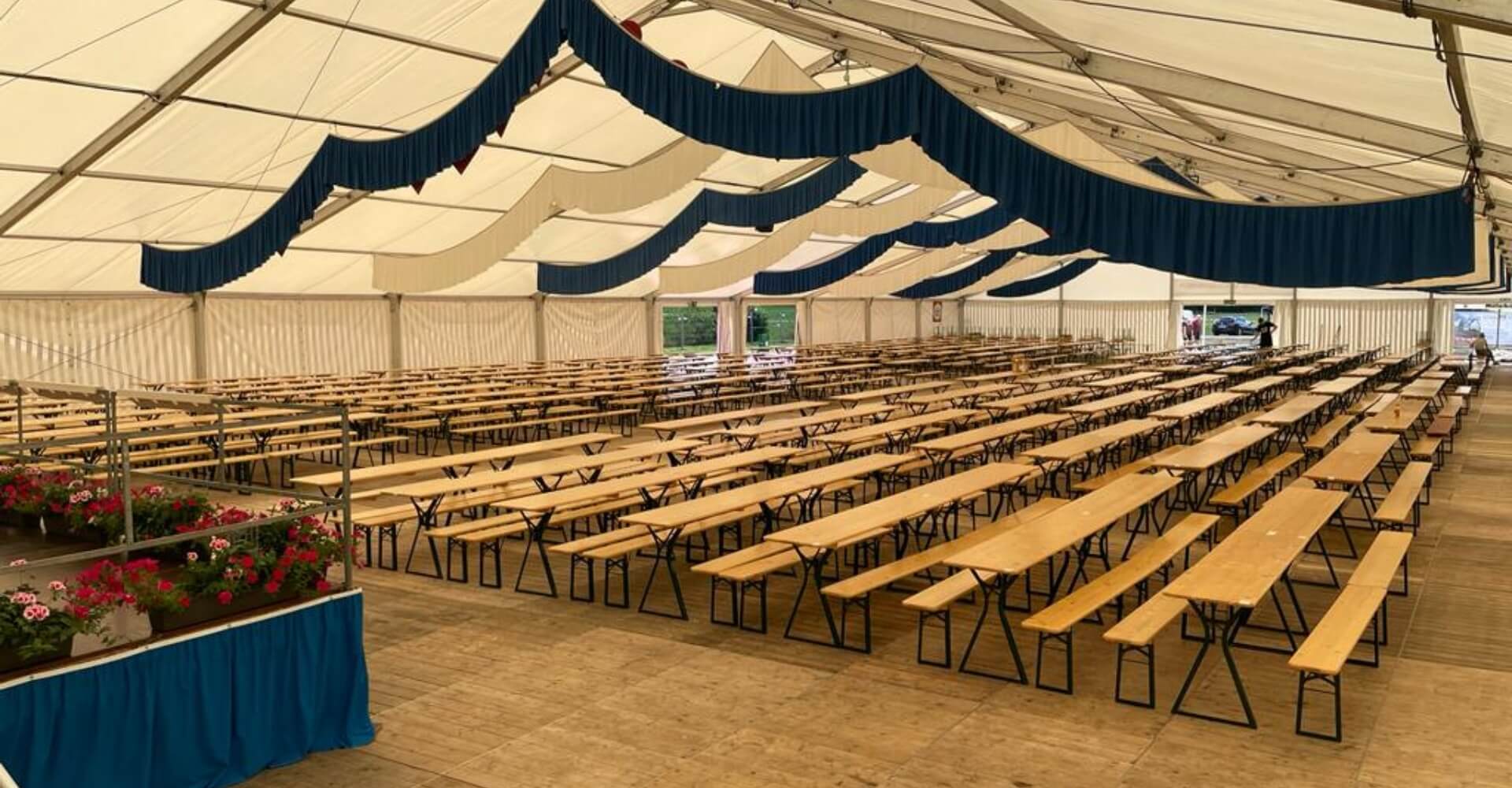 Many beer garden table sets with legroom are placed in a marquee.