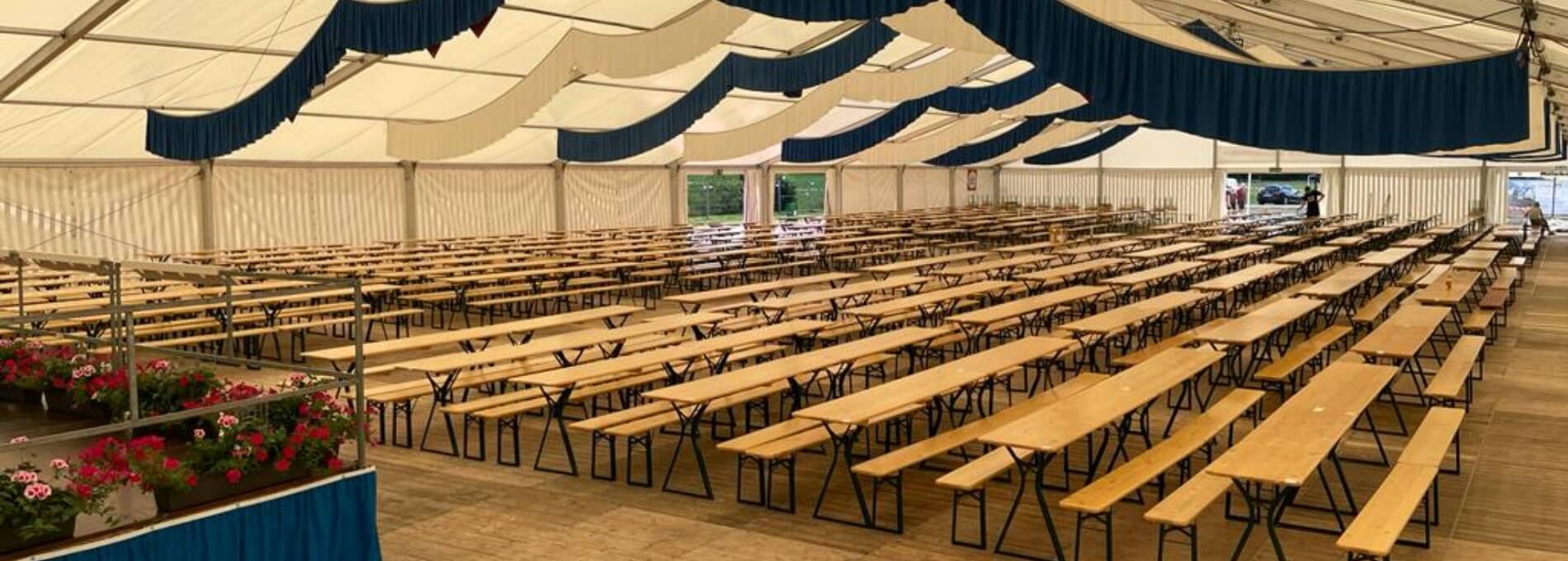 Beer garden table sets with legroom are placed in a marquee.
