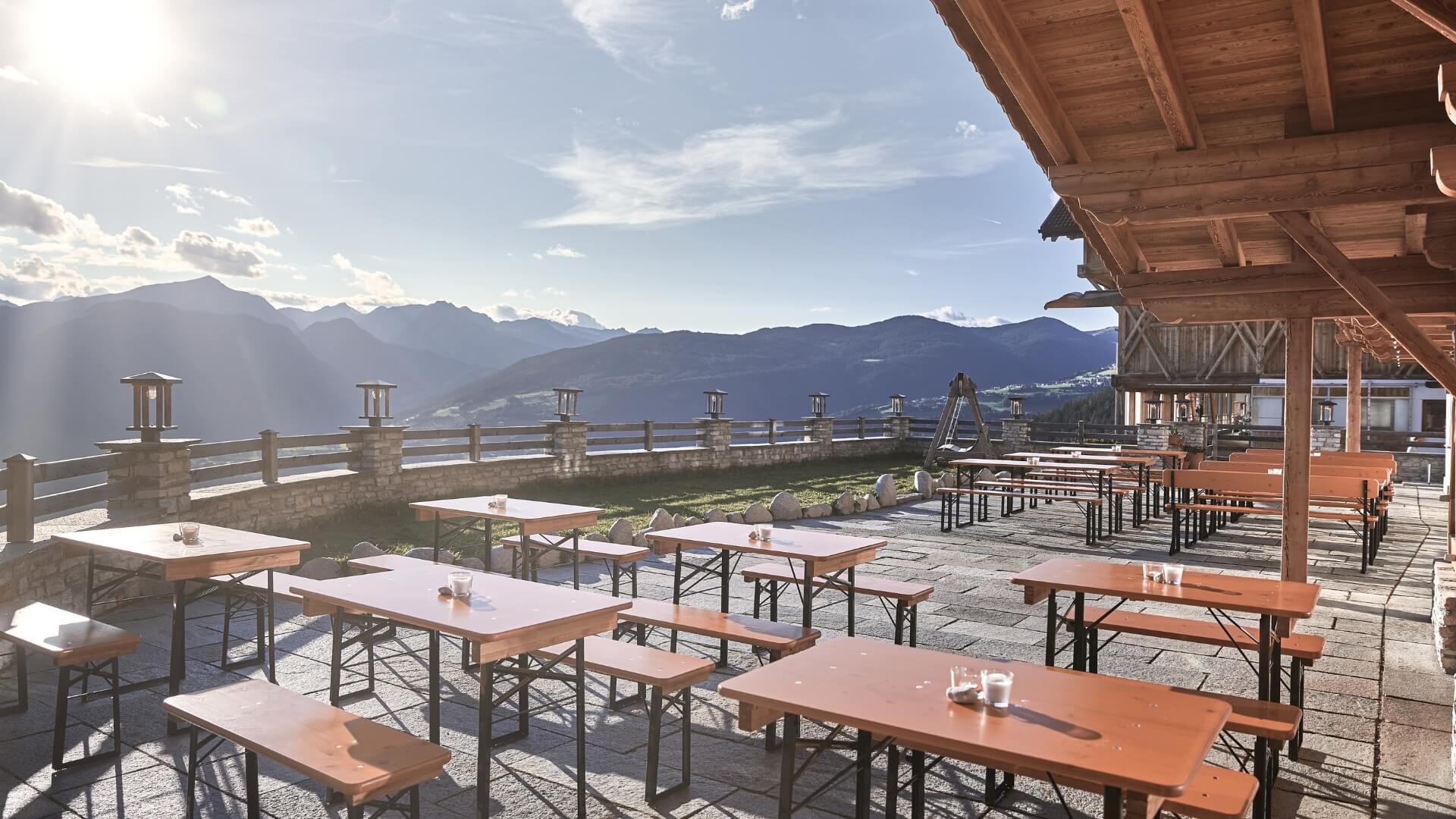 On a terrace of a cottage are small beer garden table sets in the sun.