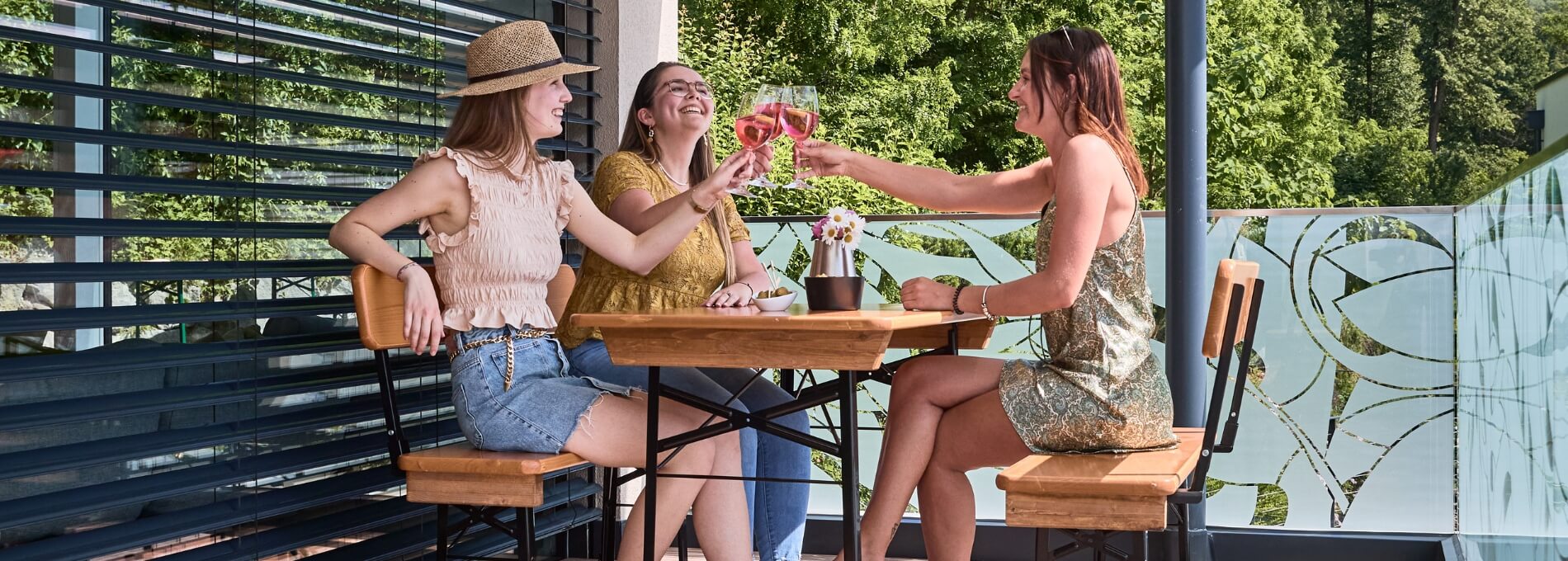 Friends sit together on the small beer garden table set Shorty with backrest and enjoy drinks on the terrace.