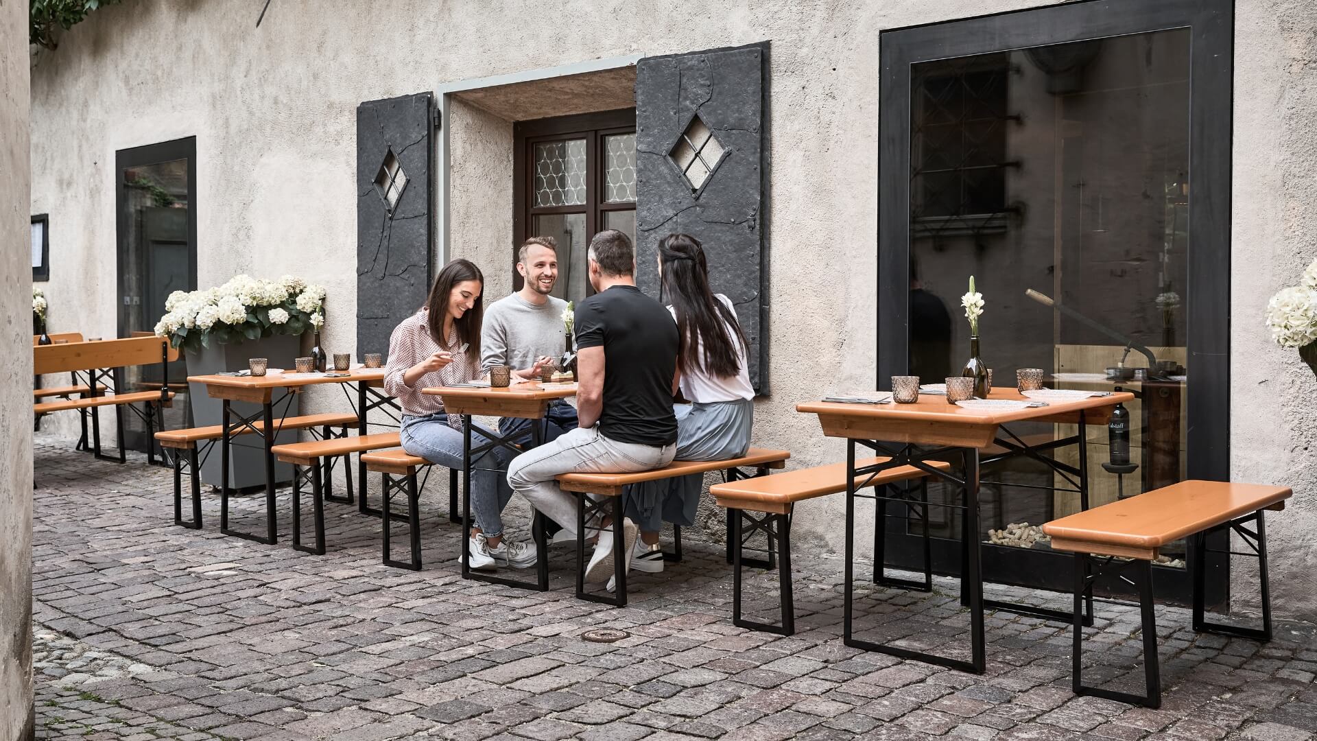 Four people are sitting on the small beer garden table set in the outdoor area of a  restaurant.