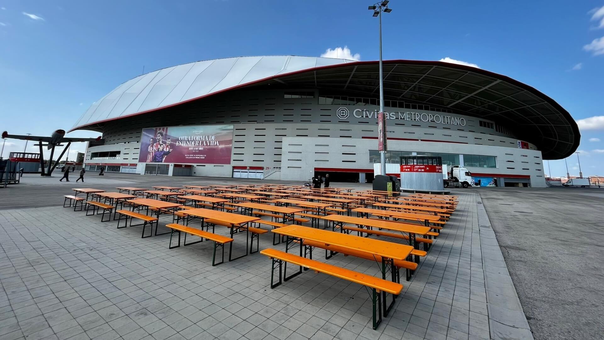 Classic beer garden table sets are set up in front of the Atletico de Madrid stadium.