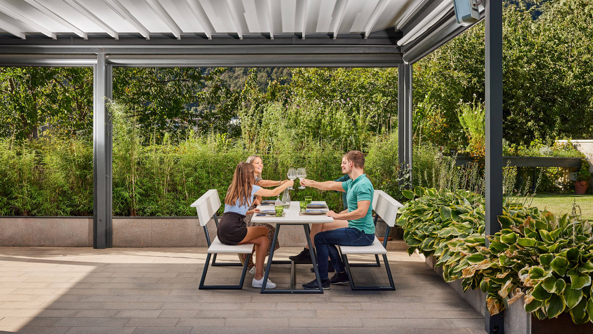 Vier Personen genießen das Essen im Außenbereich auf der Designgarnitur Riva und stoßen mit Gläsern an.