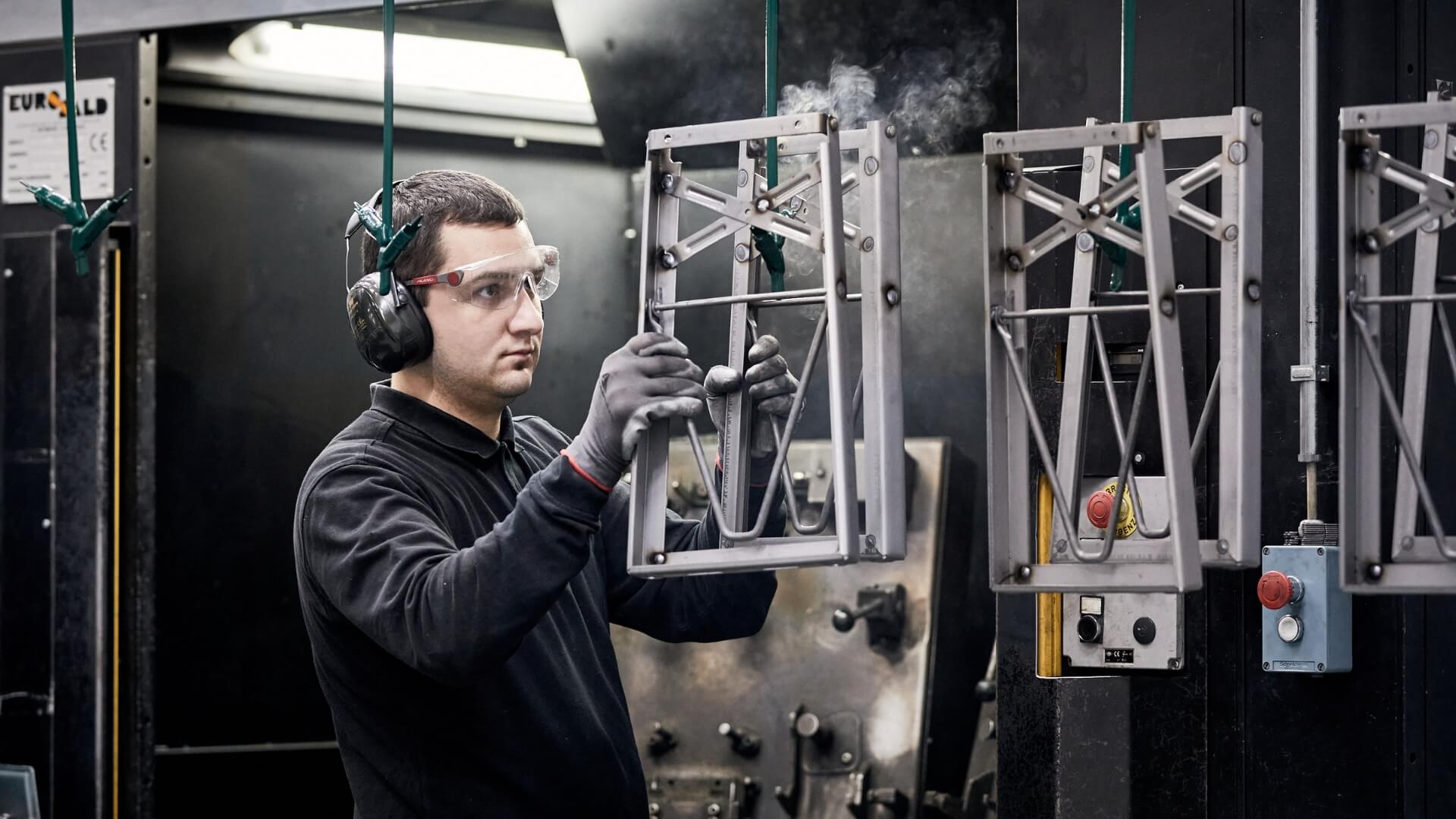 A production worker hangs up the base frame for powder coating.