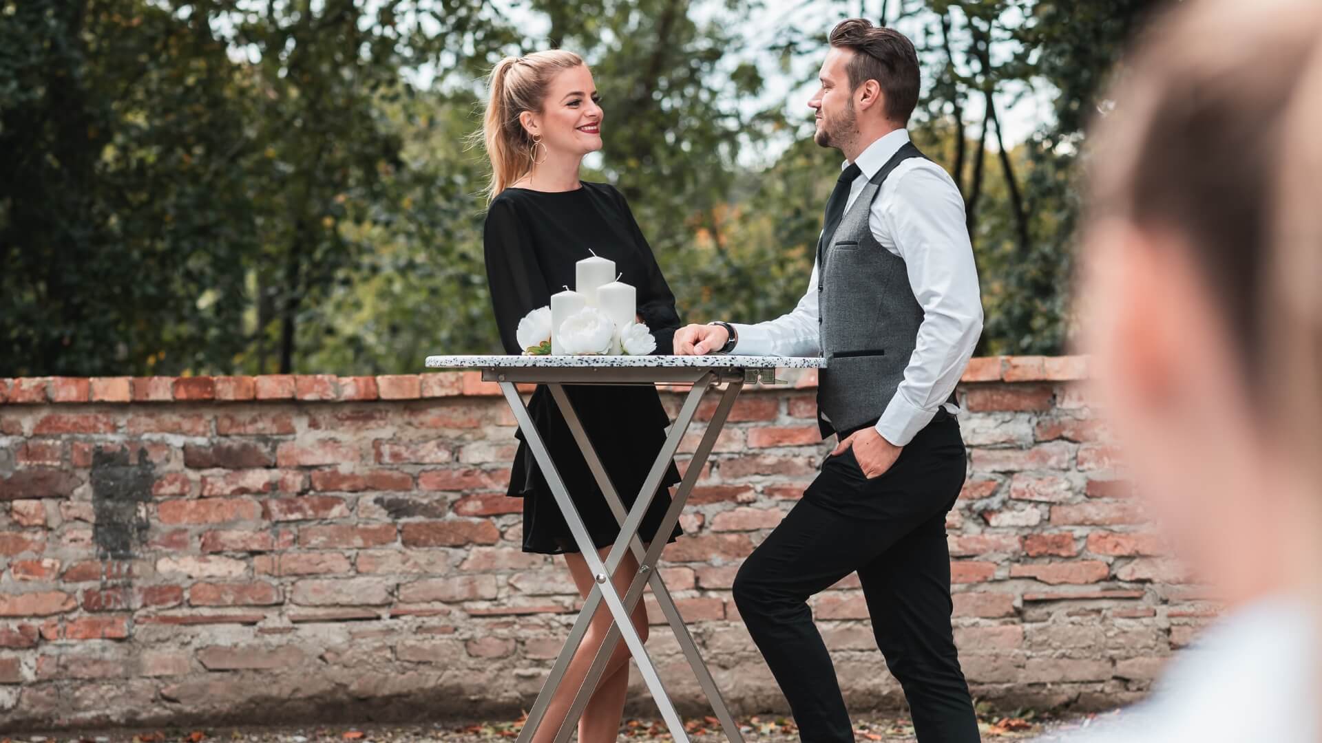 Two people standing outside at the poseur table.