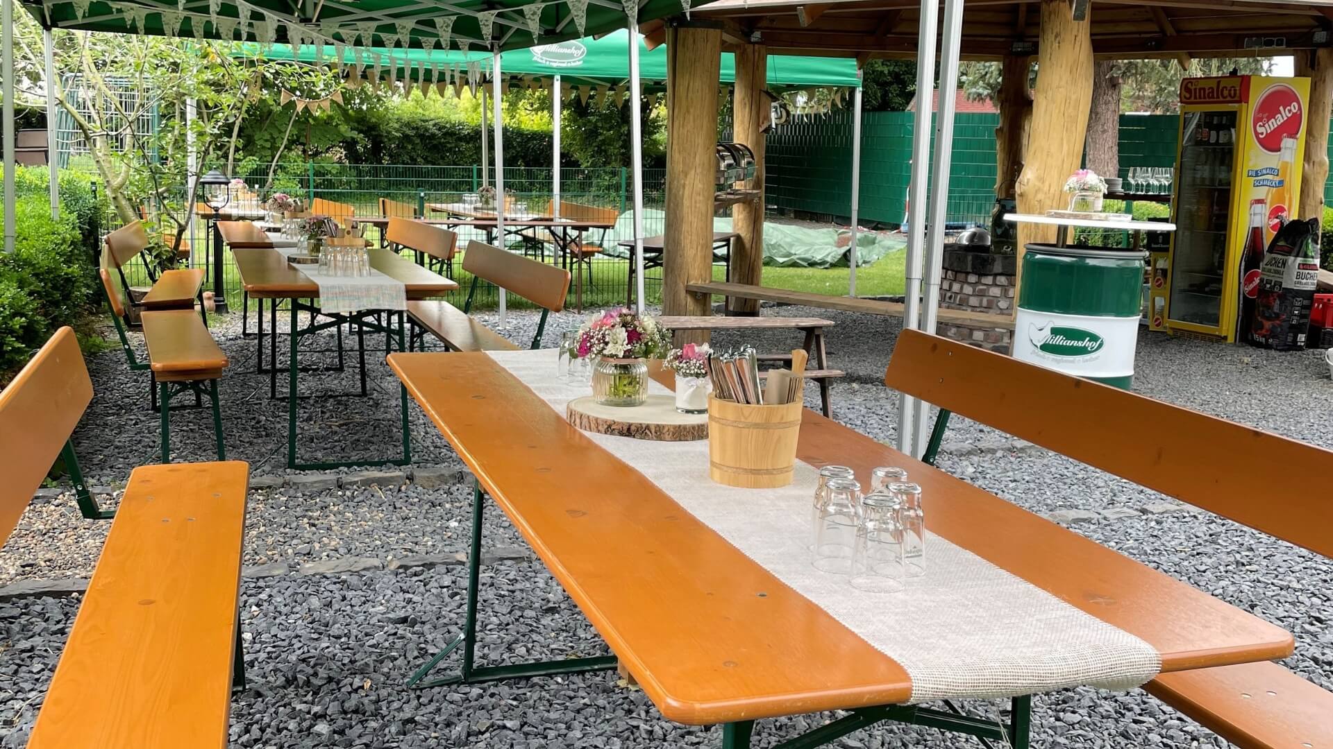 For an event at the Milianshof, wide beer garden table sets with backrests were decorated and set up outside under a folding pavilion.