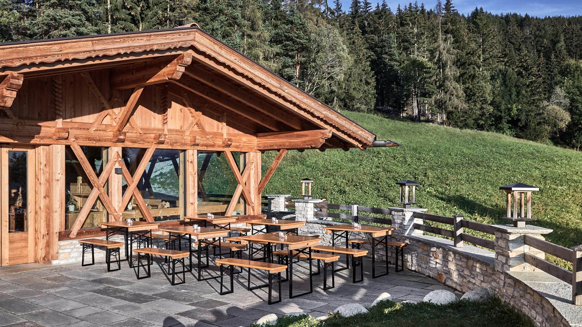 Mehrere kleine Bierzeltgarnituren sind auf der Alm aufgestellt.