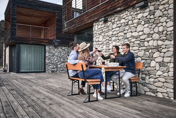 Vier Personen essen zu Mittag auf einer kleinen Bierzeltgarnitur mit Lehne auf der Terrasse.