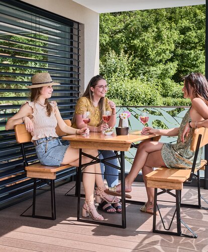 Freunde sitzen gemeinsam auf der kleinen Bierzeltgarnitur Shorty mit Lehne und genießen Getränke auf der Terrasse.