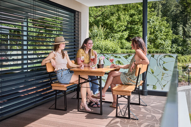 Freunde sitzen gemeinsam auf der kleinen Bierzeltgarnitur Shorty mit Lehne und genießen Getränke auf der Terrasse.