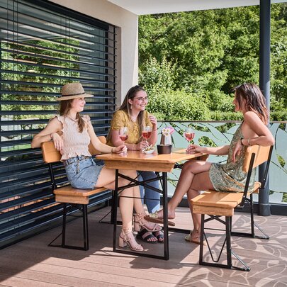 Freunde sitzen gemeinsam auf der kleinen Bierzeltgarnitur Shorty mit Lehne und genießen Getränke auf der Terrasse.