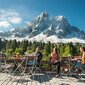 Mehrere Personen sitzen auf einer Terrasse auf den Biergartenmöbel mit Blick auf die Berge.
