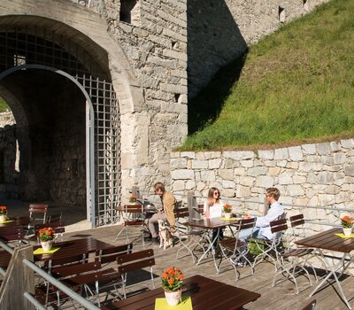 Ein paar Personen sitzen draußen auf den rechteckigen Biergartenmöbel und genießen die Sonne.