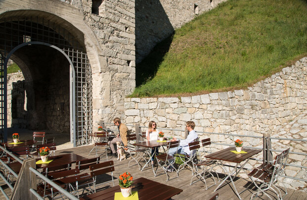 Ein paar Personen sitzen draußen auf den rechteckigen Biergartenmöbel und genießen die Sonne.