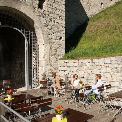 Ein paar Personen sitzen draußen auf den rechteckigen Biergartenmöbel und genießen die Sonne.