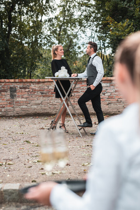 Two people are served at a folding bar table covered with a tablecloth.
