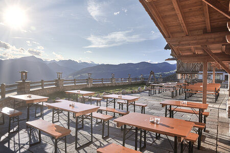 On a terrace of a cottage are small beer garden table sets in the sun.