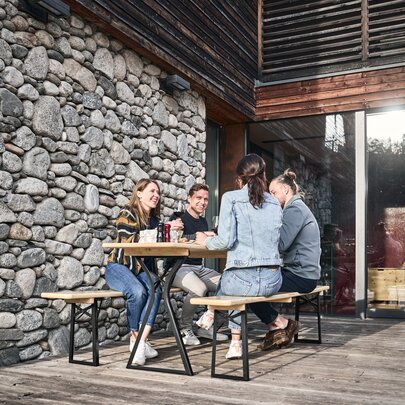 Vier Personen sitzen auf der Bierzeltgarnitur in Beinfreiheit in Natur auf einer Terrasse.