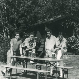 4 Personen stehen neben einer Bierzeltgarnitur. Ein Schwarz-Weiß-Foto das in Bezug steht zum Produktionsstart der Bierzeltgarnituren im Jahre 1986.