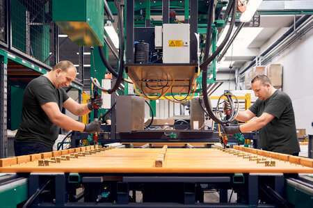 Two employees use a machine to assemble the locking mechanisms on several RUKU1952 beer benches.