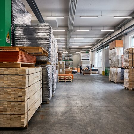 Ein Foto des Inneren der Produktionshalle in Schabs, links und rechts sieht man verpackte Bierzeltgarnituren und am Ende der Halle sieht man zwei Mitarbeiter.