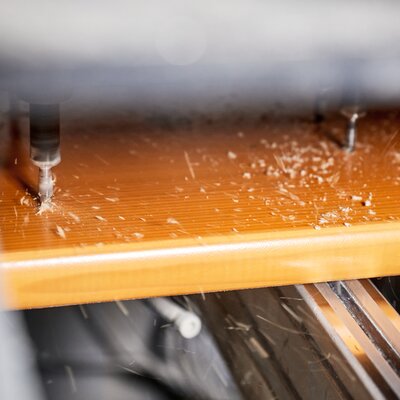 Auf dem Foto ist zu sehen, wie eine Maschine die Bohrlöcher für die spätere Montage der Untergestelle und Verschlussmechanismen in eine Bierbank einbringt.