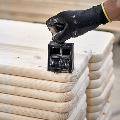 Auf dem Bild sieht man einen Stapel noch nicht fertiger Bierbänke. Ein Mitarbeiter ist gerade dabei, mit einem Stempel Personalisierungen auf dem Holz anzubringen.