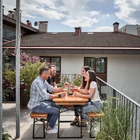 4 Personen sitzen auf einer kurzen Bierzeltgarnitur auf der Terrasse und haben eine Menge Spaß.