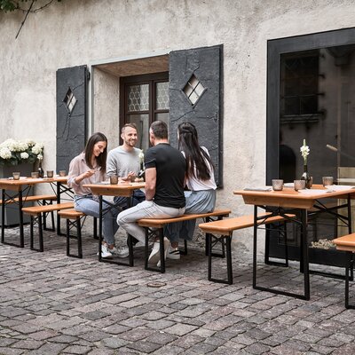 Vier Personen sitzen auf der kleinen Bierzeltgarnitur im Außenbereich eines Lokals.