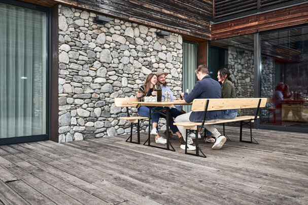 Vier Personen essen zu Mittag auf einer Bierzeltgarnitur mit Lehne auf der Terrasse.