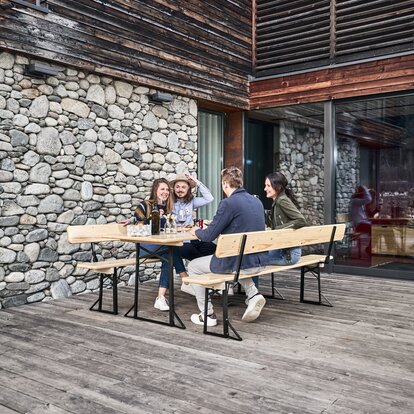Vier Personen essen zu Mittag auf einer Bierzeltgarnitur mit Lehne auf der Terrasse.