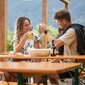 Ein Paar stoßt mit zwei Bierkrügen zusammen und sitzt dabei auf klassische Bierzeltgarnituren.
