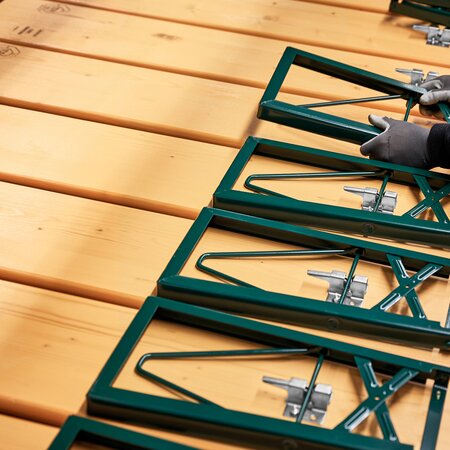 The image shows the assembly of the underframes onto the beer benches. An employee is placing an underframe onto a prepared bench, getting it ready for the next step.